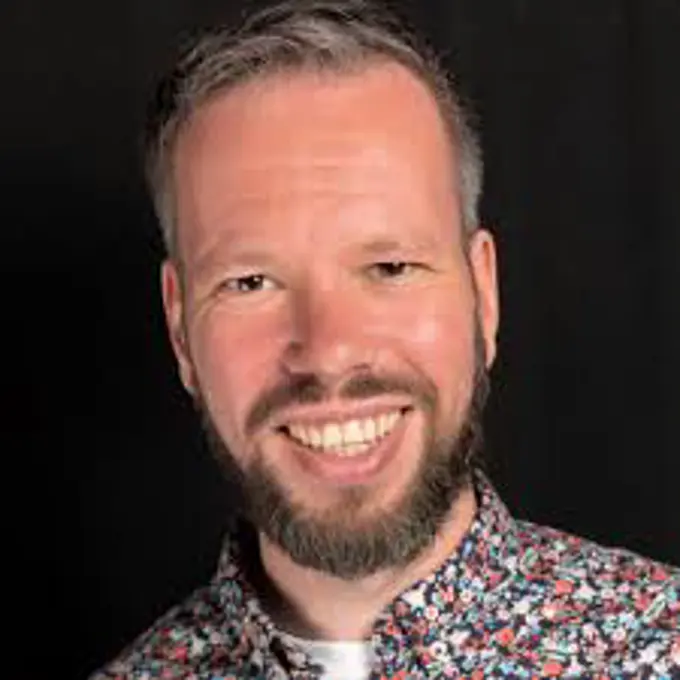 Sebastiaan wears a floral shirt and is smiling at the camera, against a black background