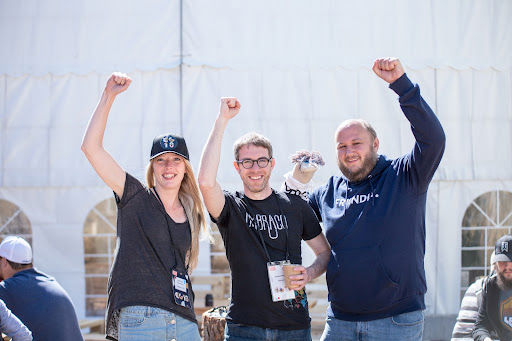 Three white people raising their fists and smiling against a white tent background