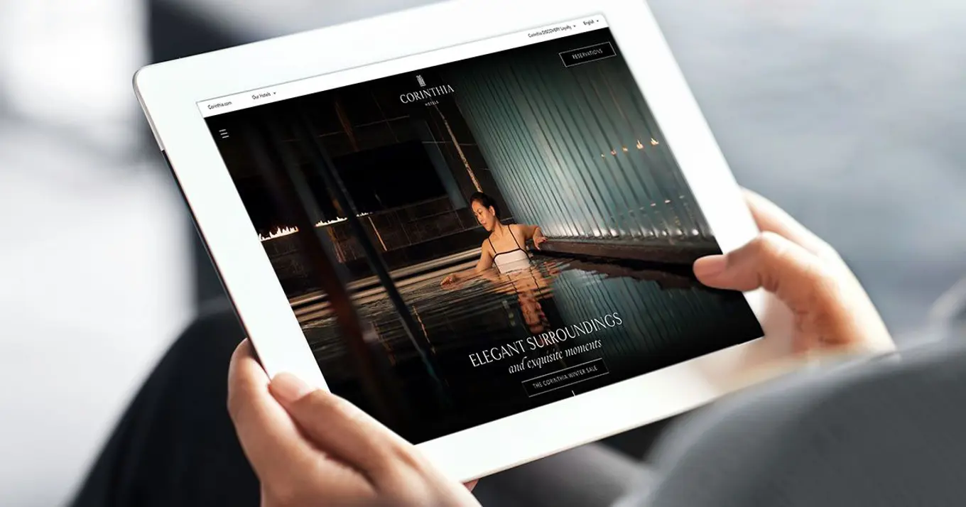 A person holding a tablet displaying Corinthia Hotels' website