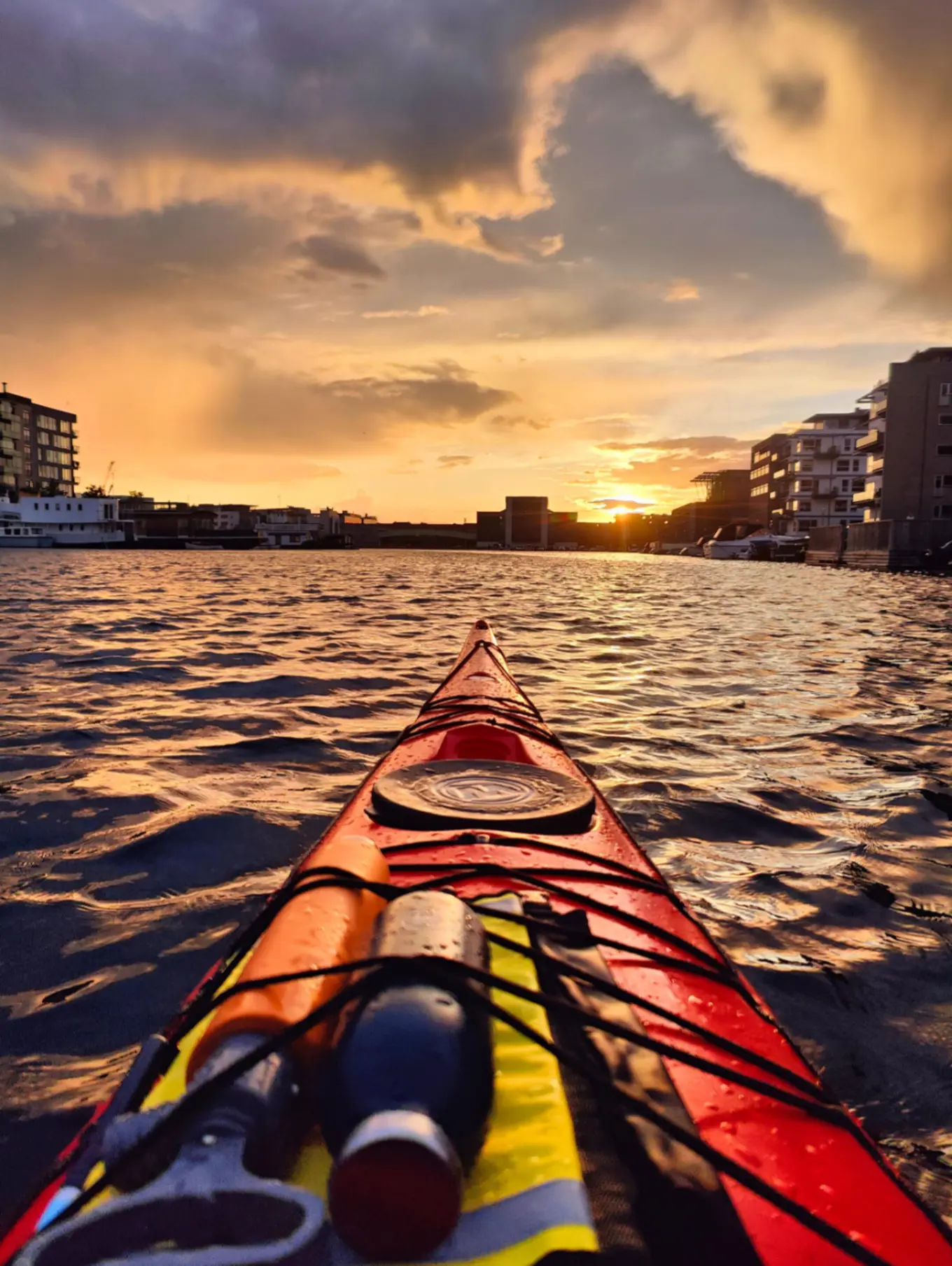 Image of the view from a kayak in Copenhagen harbour as sunset, with a moody sky and gentle waves of water