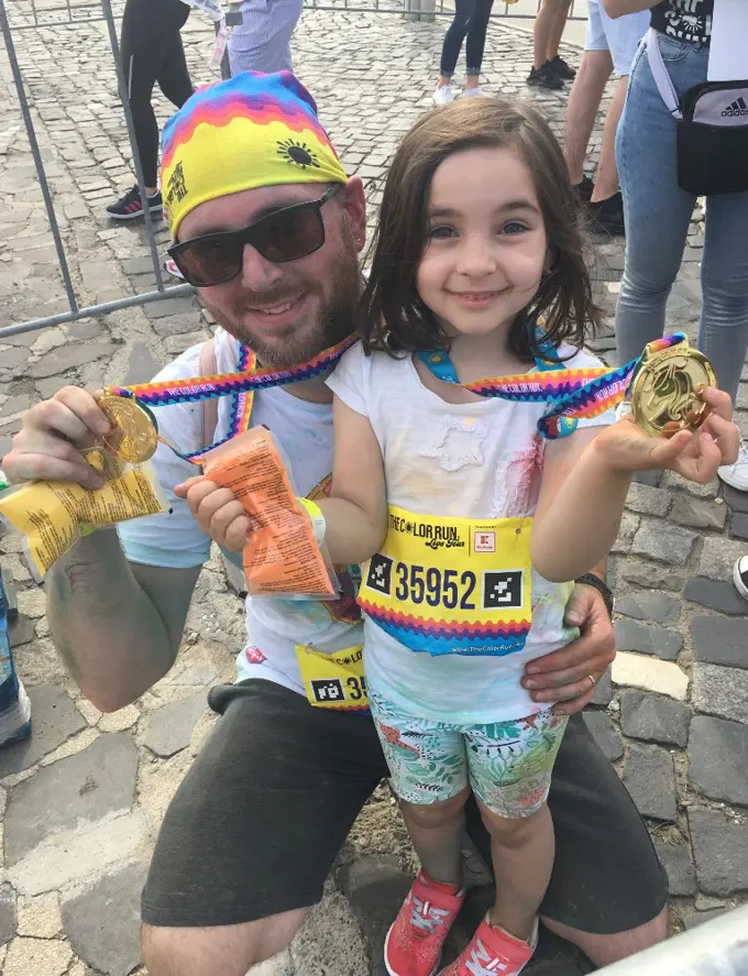 Adrian and his daughter dressed up to run wearing colorful clothing and medals