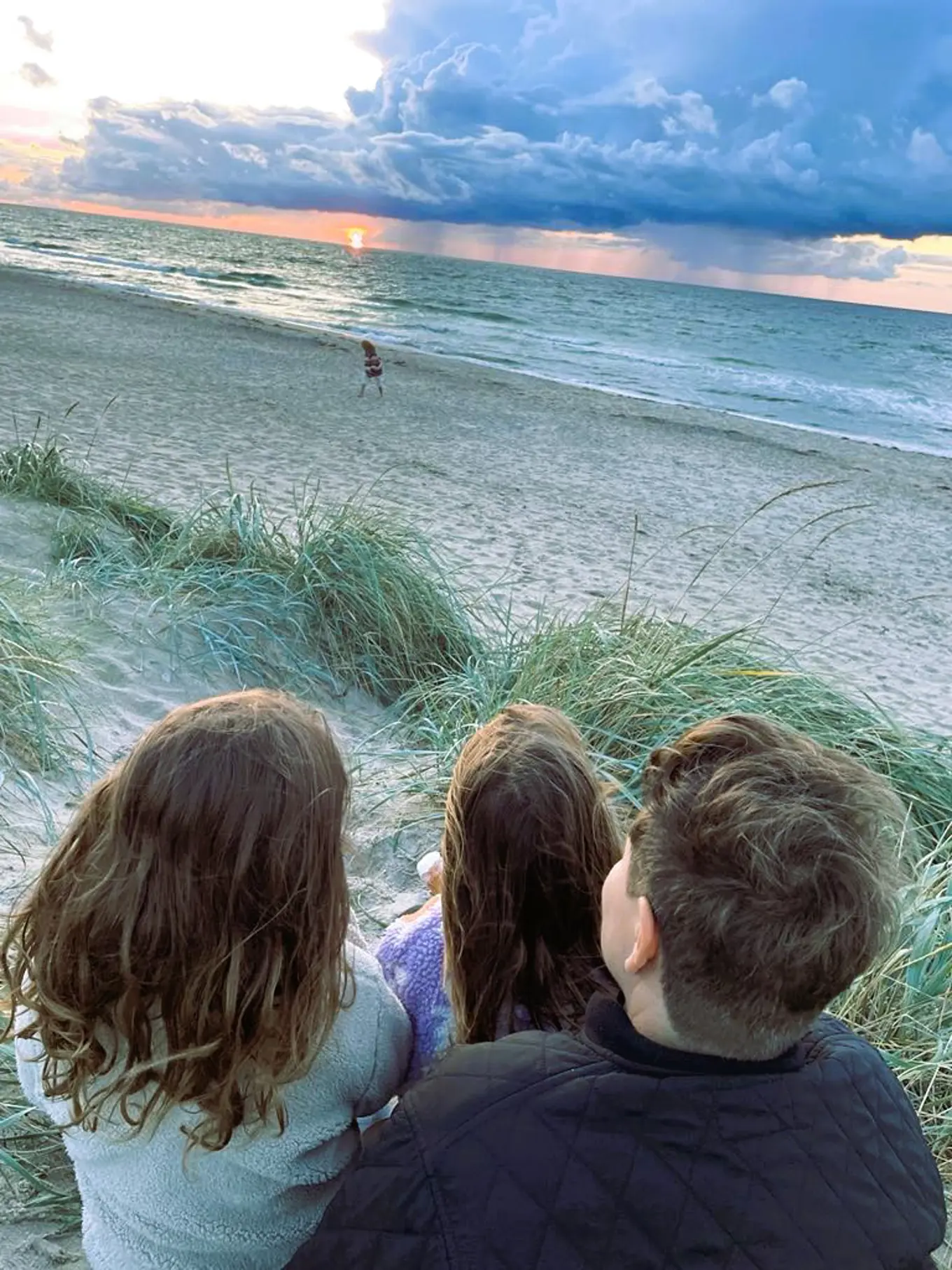 Amalie with her children on the beach, watching the sunset and rainclouds in the distance