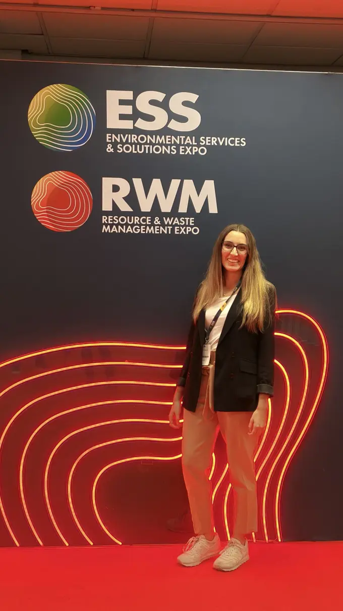 A woman standing in front of a sign at the Recycling and Waste Conference in Birmingham, UK)
