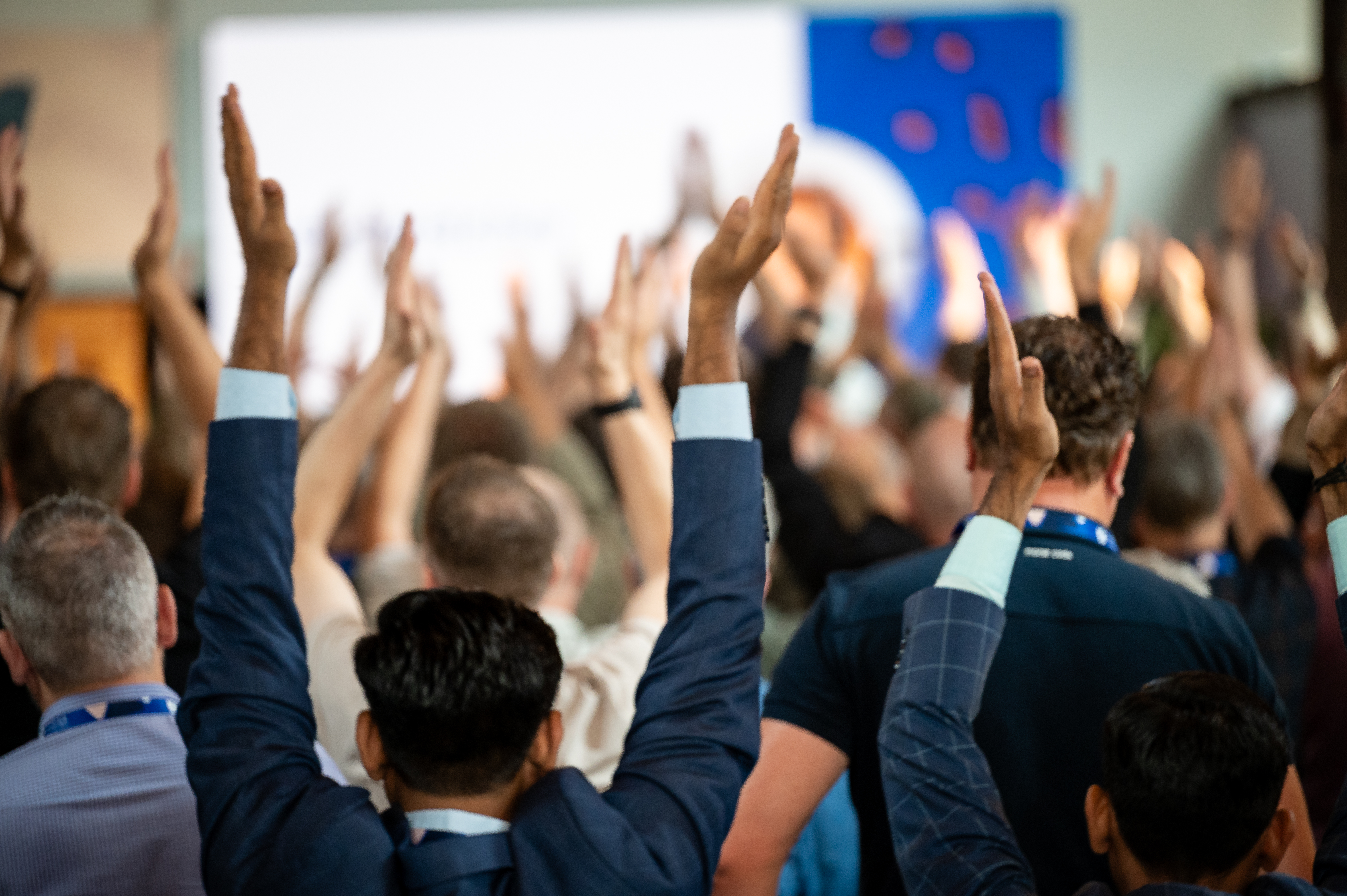 Crowd in a stadium cheering with hands raised while people stand in the foreground