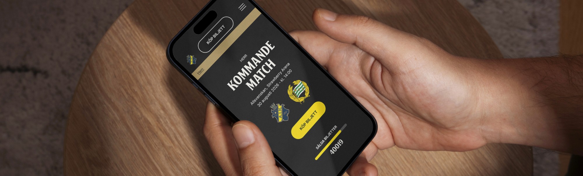 Hand holding a smartphone showing “KOMMANDE MATCH” and “KÖP BILJETT” ticket text.