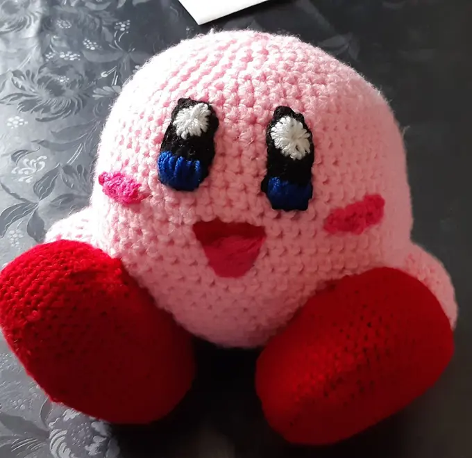 A crocheted pink Kirby (animated character) with big eyes and red shoes