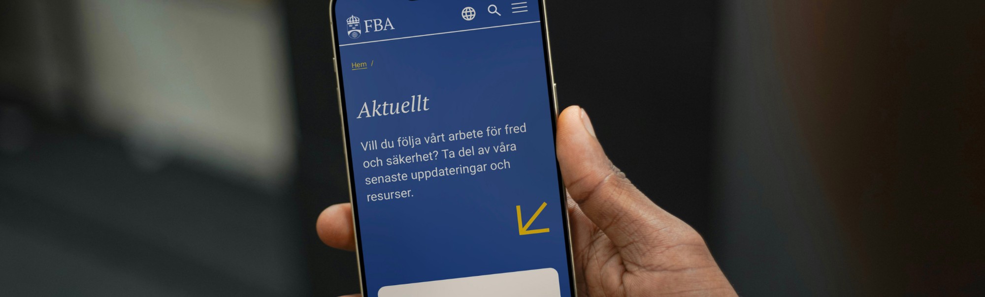 Hand holding a smartphone showing Swedish site “Aktuellt” with text and a yellow arrow down indicator