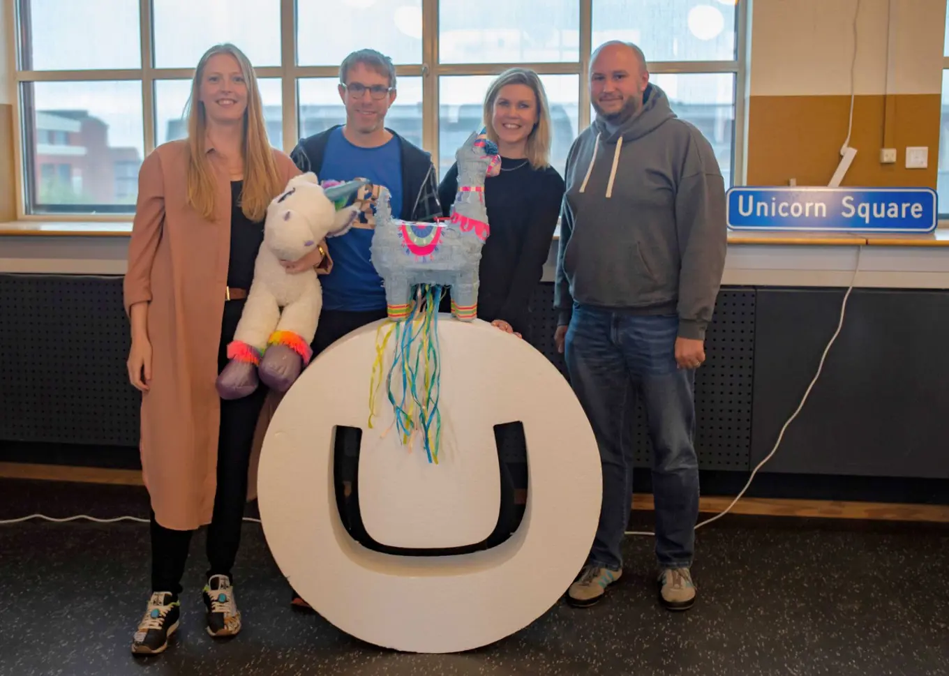 Sofie, Damiaan, Sophie and Jeavon stand together with a unicorn and llama next to a large Umbraco logo