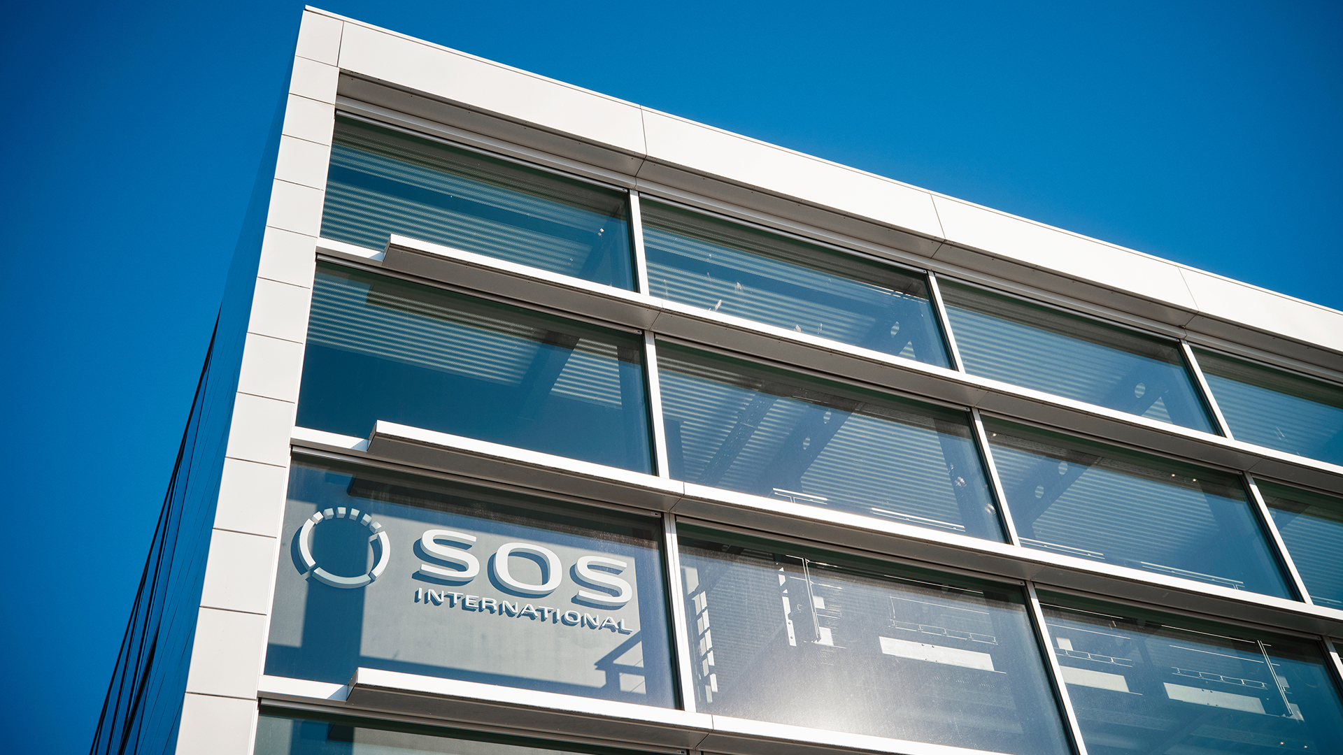 Modern SOS International headquarters building exterior displaying the company logo on glass windows against a clear sky.