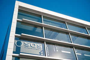 Modern SOS International headquarters building exterior displaying the company logo on glass windows against a clear sky.