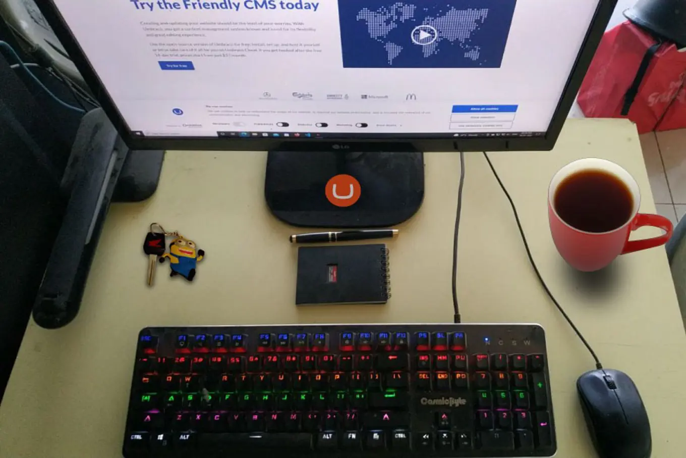 Ronak's desk, with keys, a notebook and pen, a mug of coffee, and the Umbraco front page on the screen