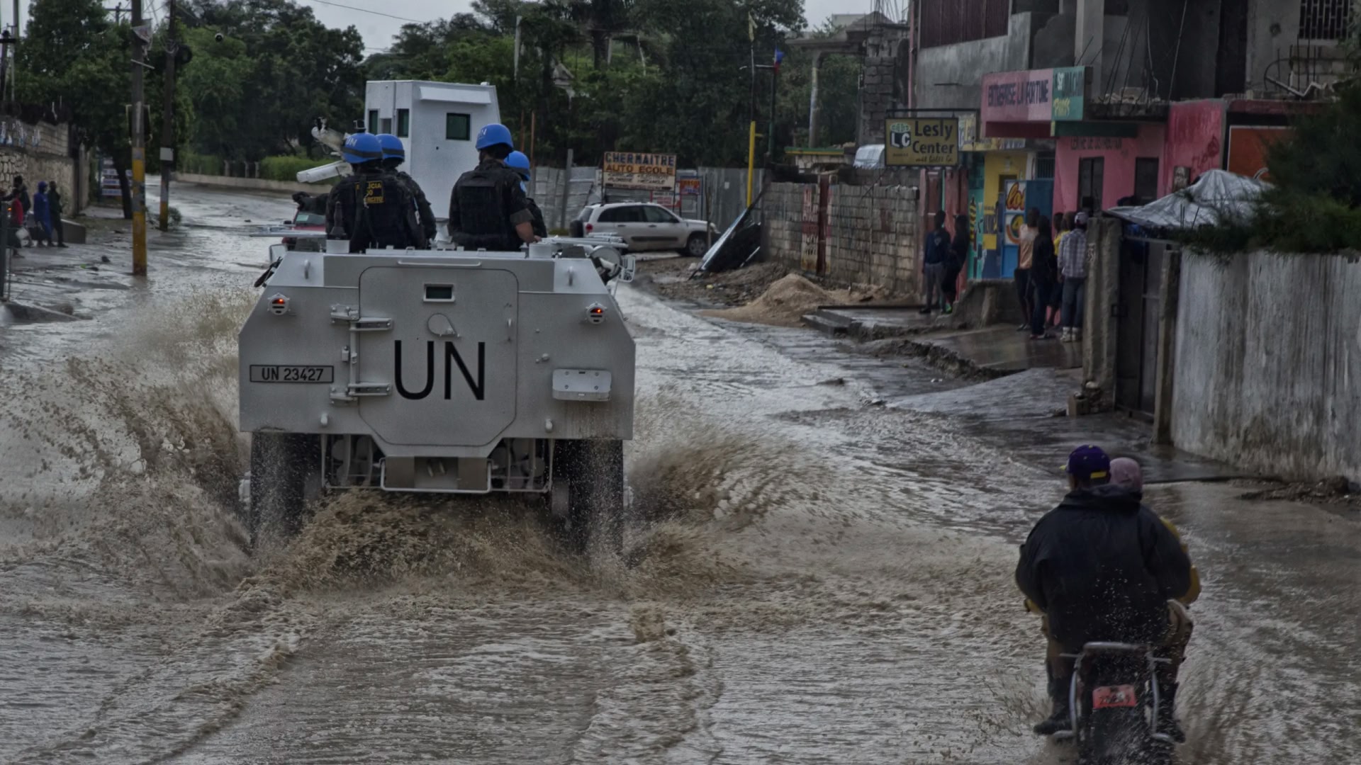 UN peacekeepers in blue helmets on an armoured vehicle driving through a flooded street