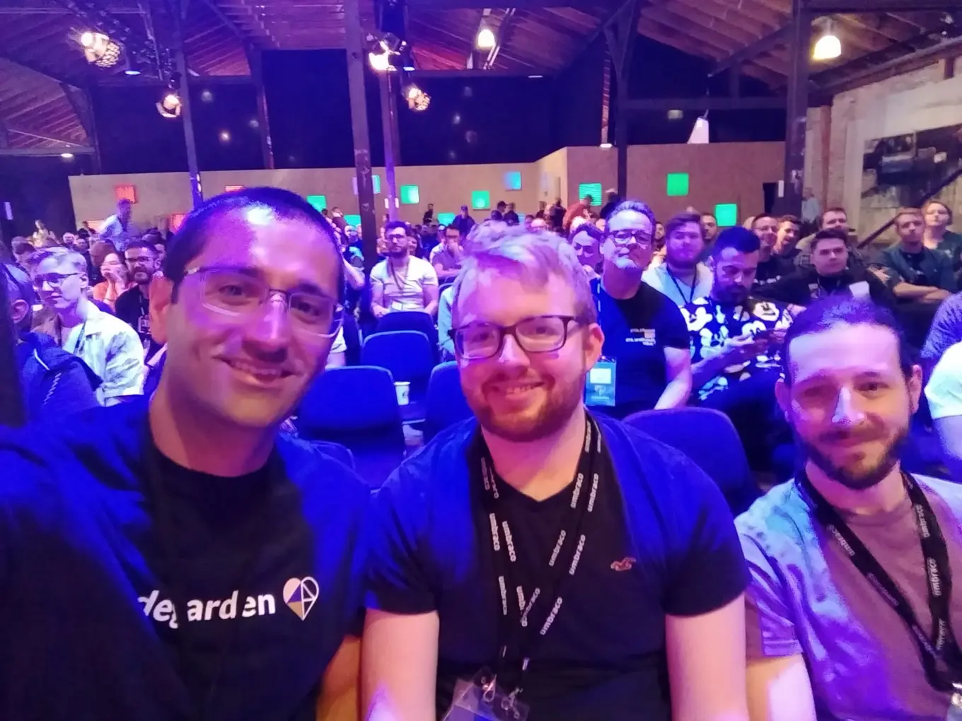 Three men take a selfie among a busy crowd of Codegarden attendees.