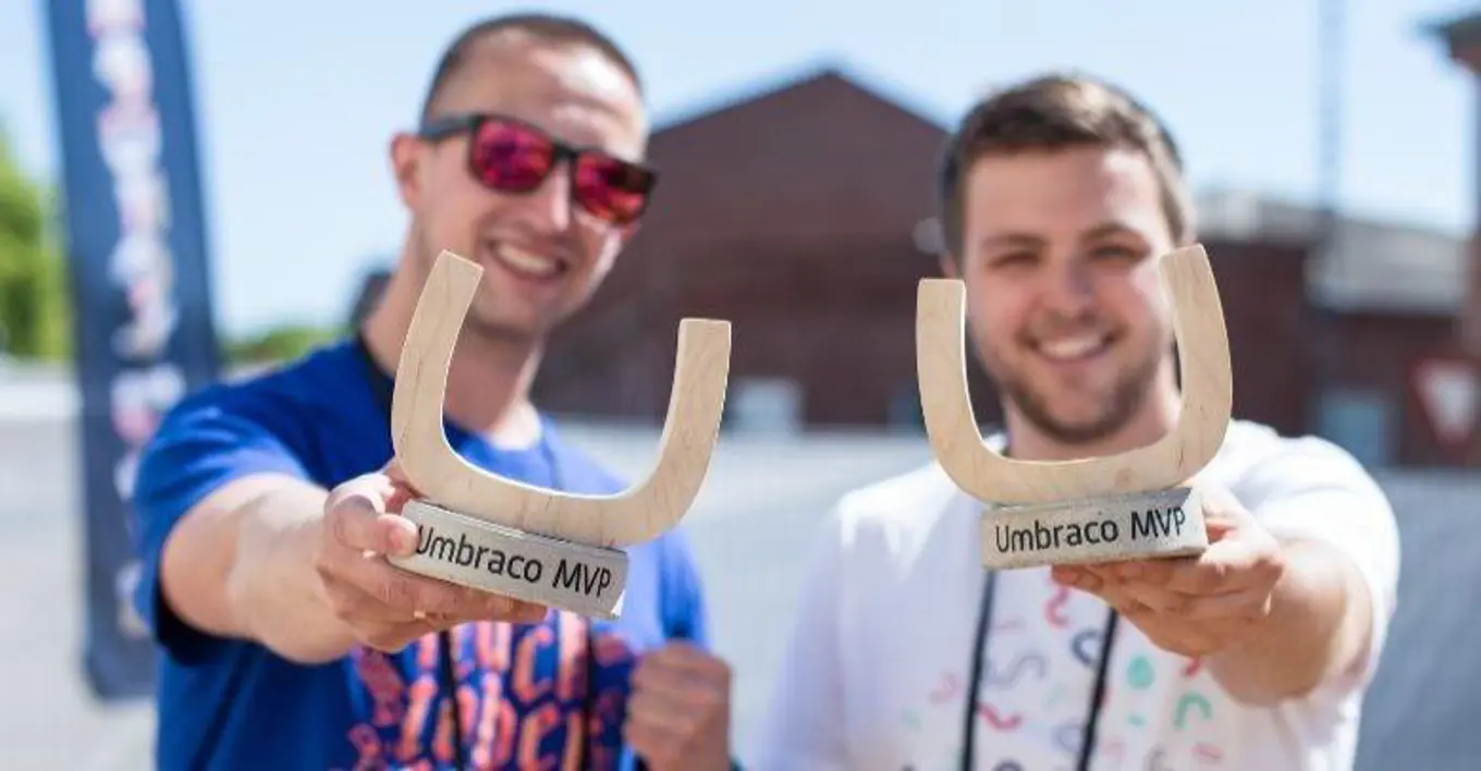 Image of two MVPs, holding MVP awards, set against a sunny, outdoor background with a blue fade text overlay, saying 2024 Umbraco MVPs