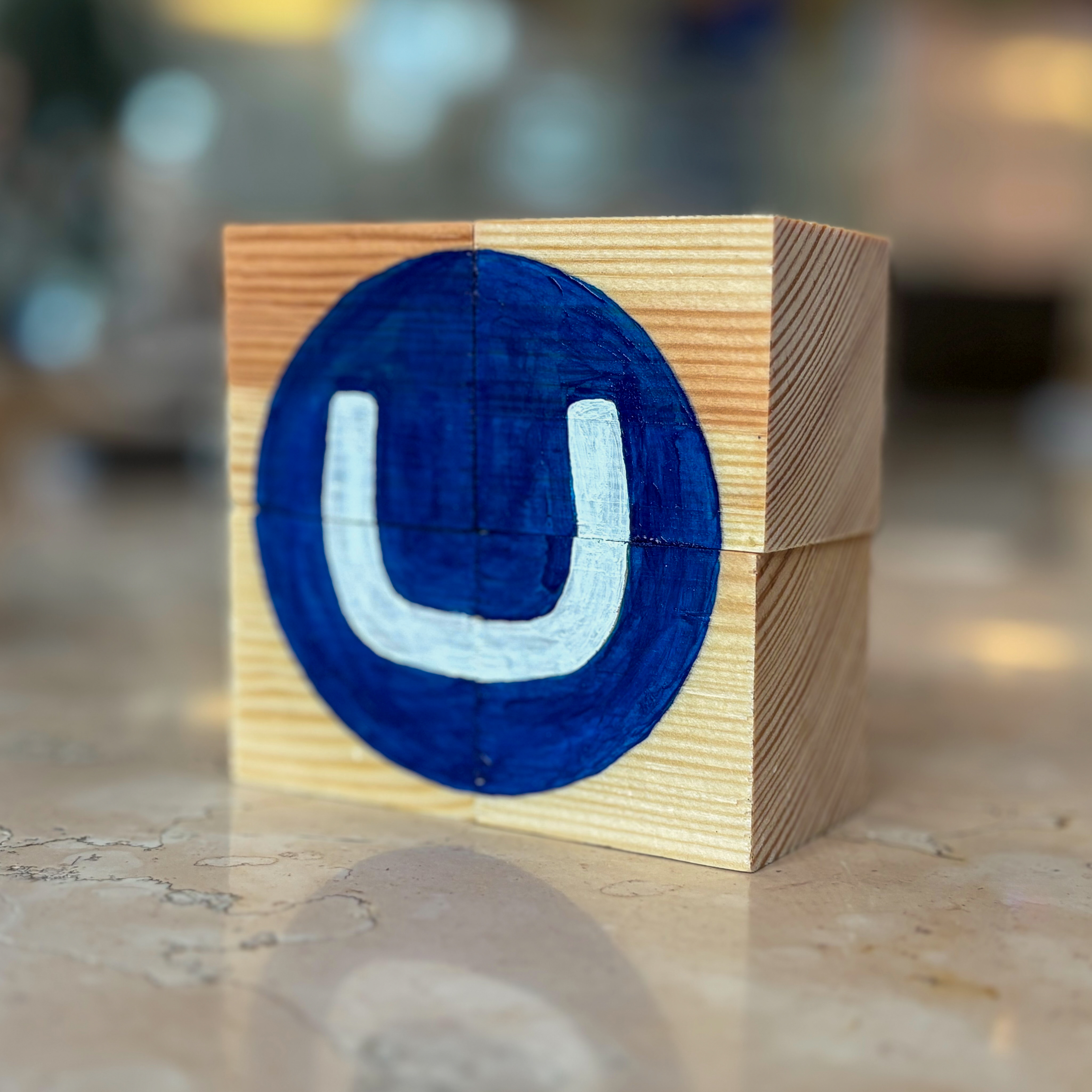 A wooden block puzzle displaying a white letter "U" inside a painted blue circle.