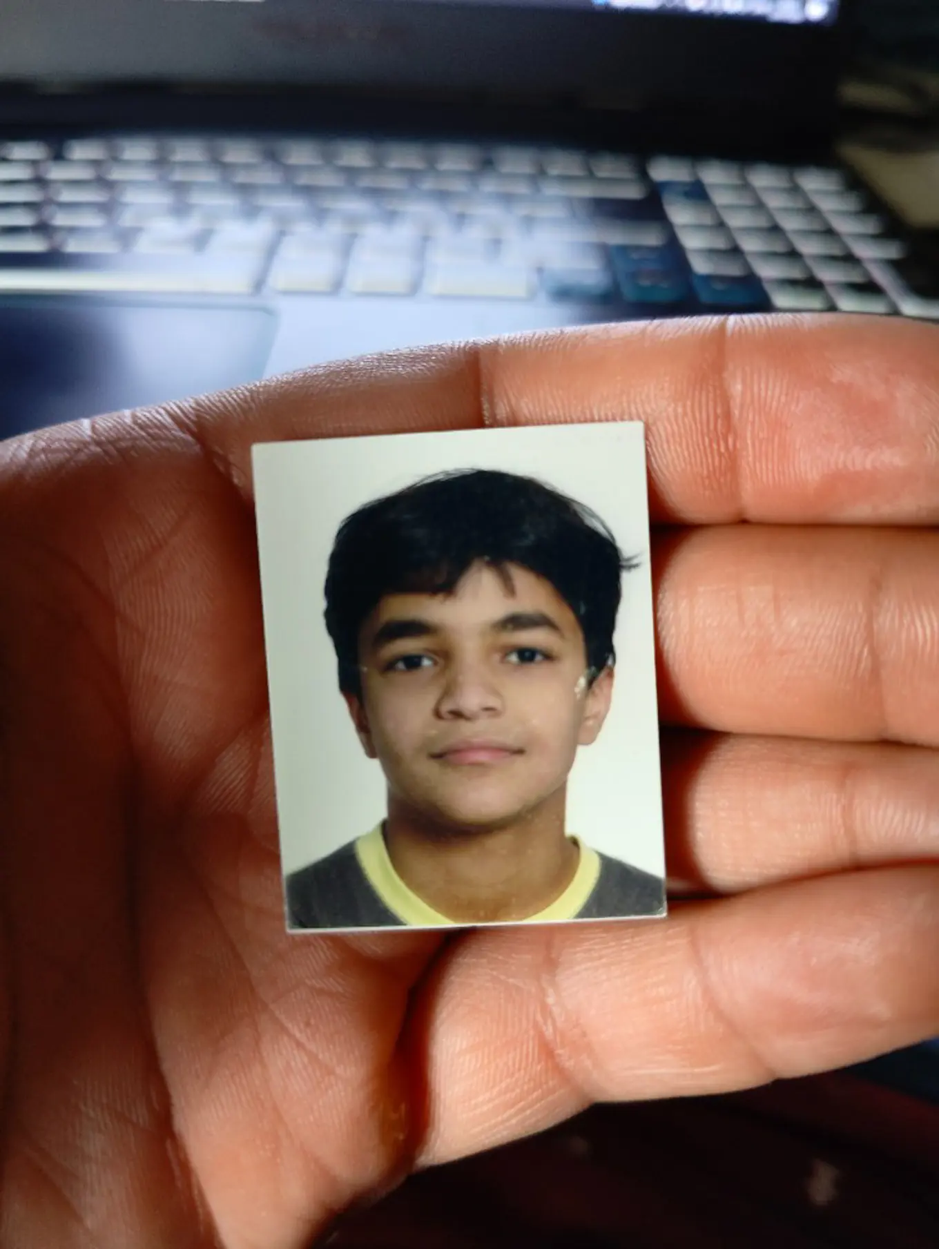 An open hand holding a rectangular headshot of a young Abdulaziz with a keyboard in the background