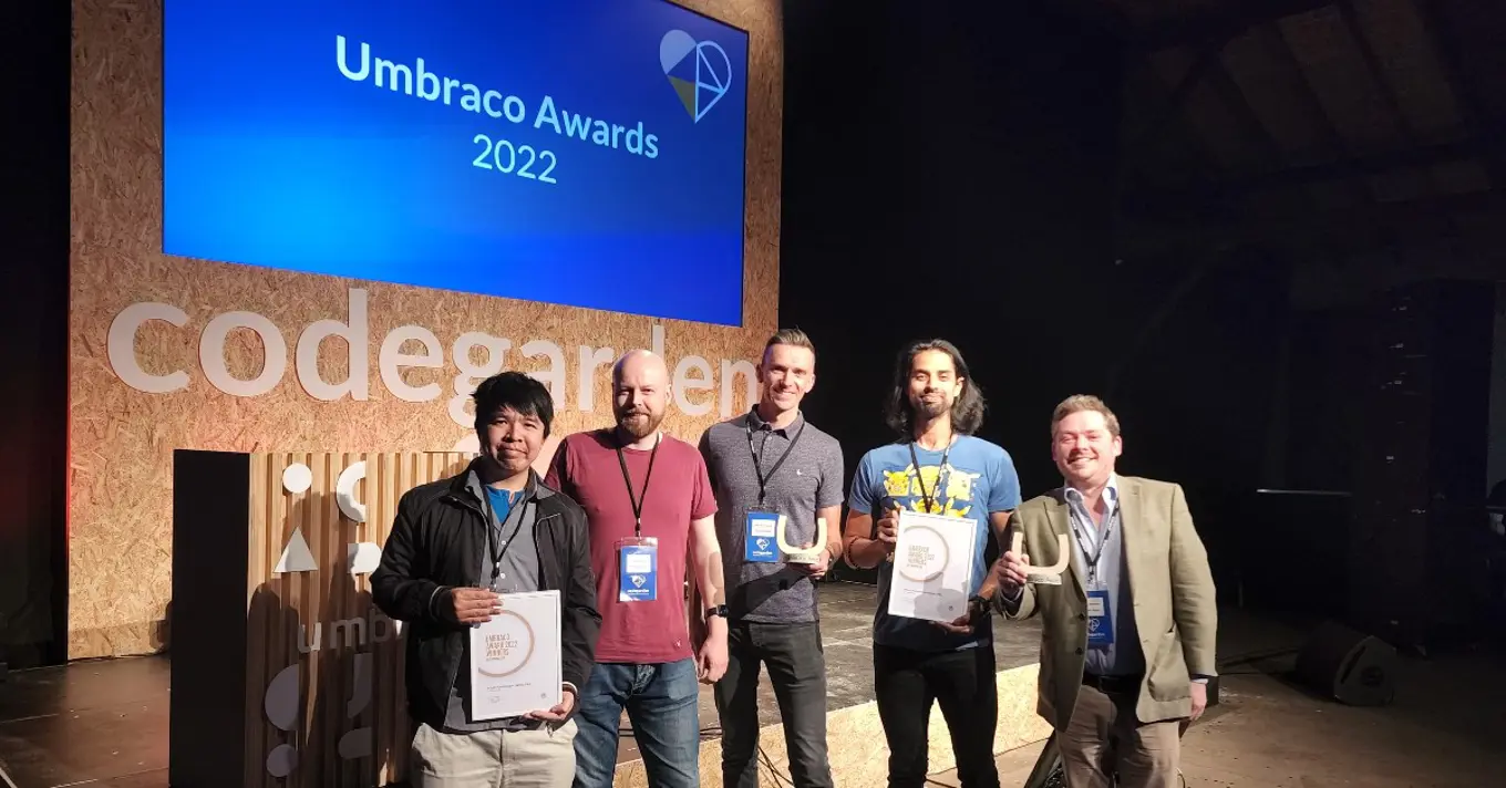 The Durable Digital team stands at the Codegarden stage displaying their framed award certificates and U statuettes.