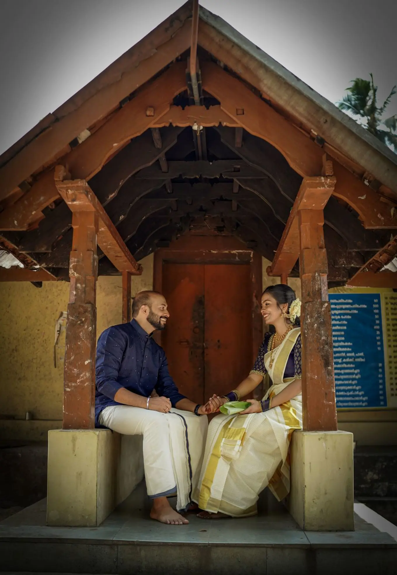 Dhanesh and his future wife, Vrindha, at their engagement celebration. Both are sat opposite on another, smiling and holding hands.