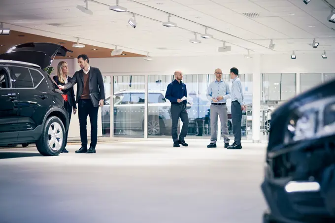 Several people standing in a car showroom