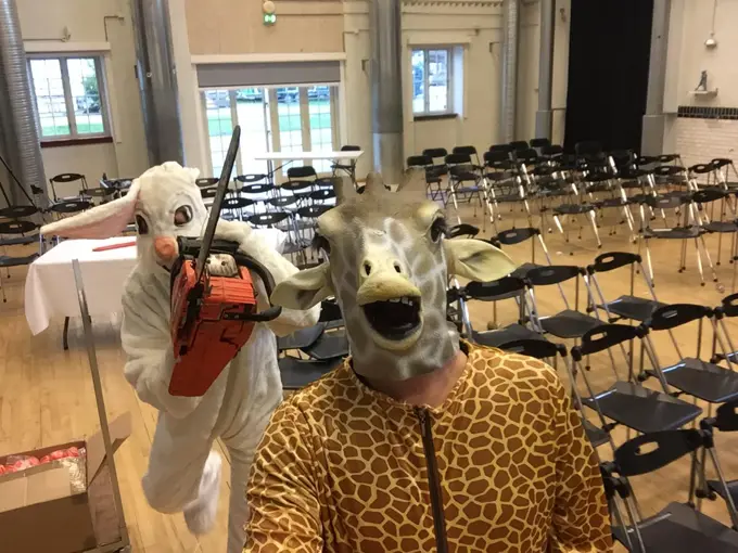 Image of two people one dressed as a rabbit holding a chainsaw and the other dressed as a giraffe