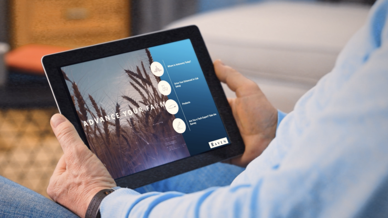 Person holding a tablet showing “ADVANCE YOUR FARM” website with navigation circles and a “RAVEN” logo