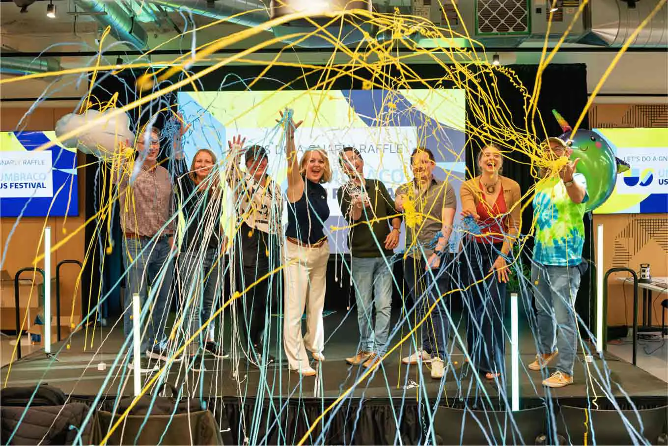 A group of Umbraco Community people celebrating a successful US Festival on stage, throwing yellow and blue streamers.