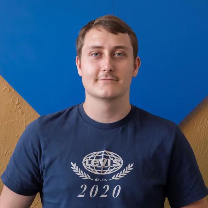 Andreas Zerbst headshot. Andreas is a white man with brown hair wearing a dark blue shirt against a blue and gold background.