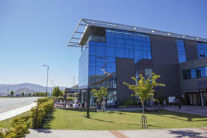 A wide exterior shot of a modern library building, featuring a blue glass facade, a manicured green lawn, and mountains in the background.
