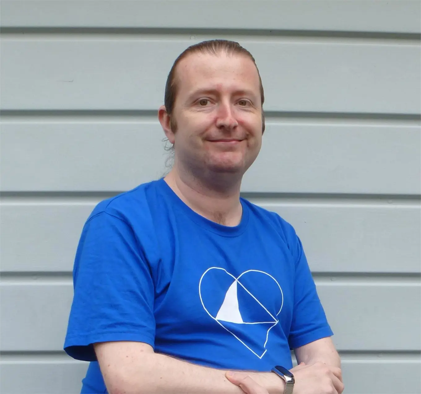 Terence Burridge wearing a royal blue tshirt with a white heart logo, in front of a grey slatted wall