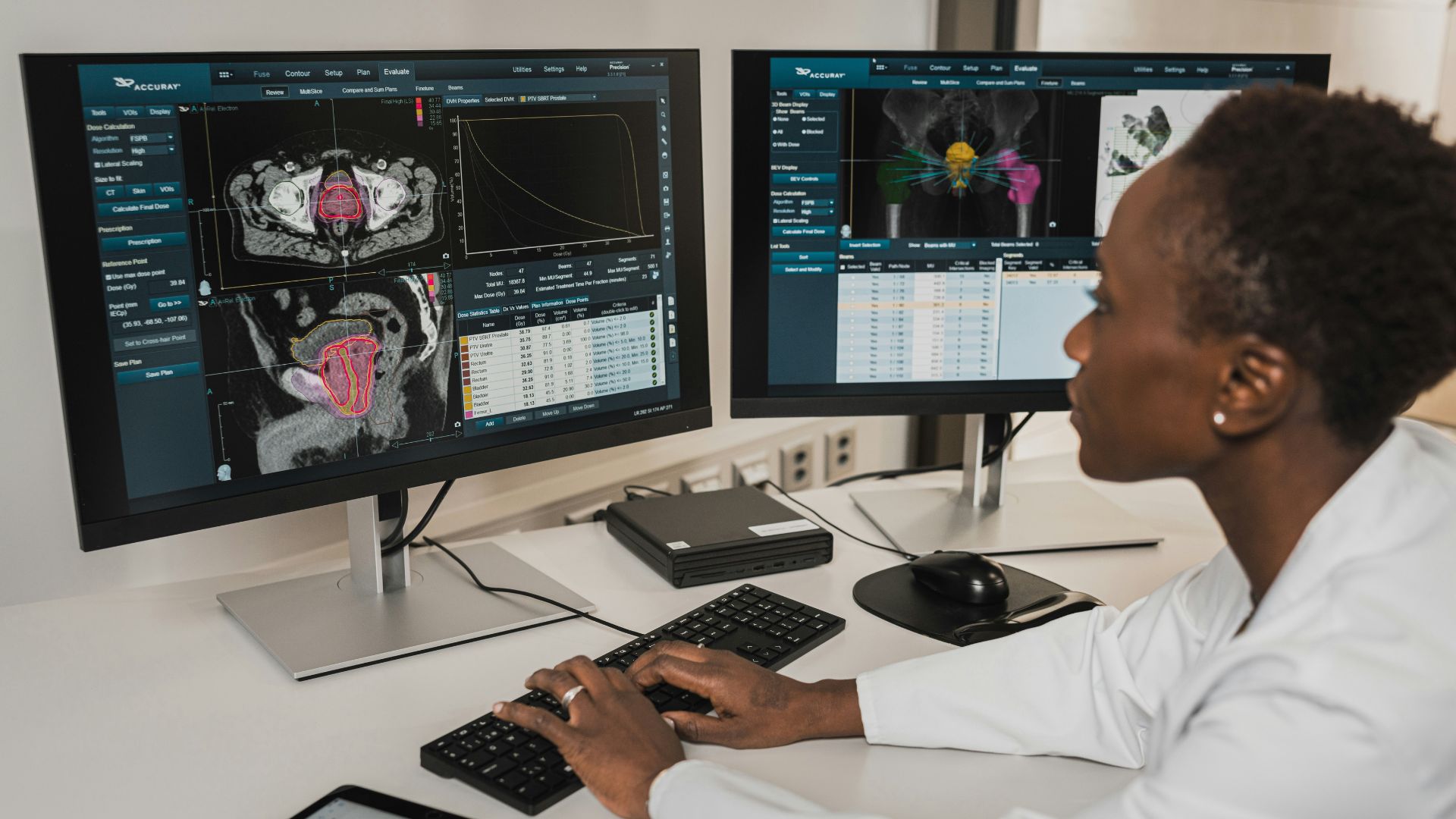 A healthcare professional working at a desk with two computer monitors displaying medical imaging scans and specialized radiology software.