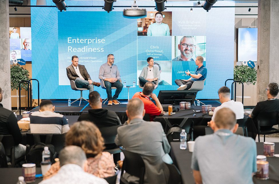A growd of four men are seated on chairs on a stage business setting