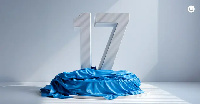 Large metallic number 17 standing behind a draped blue fabric in a bright, minimalist setting.
