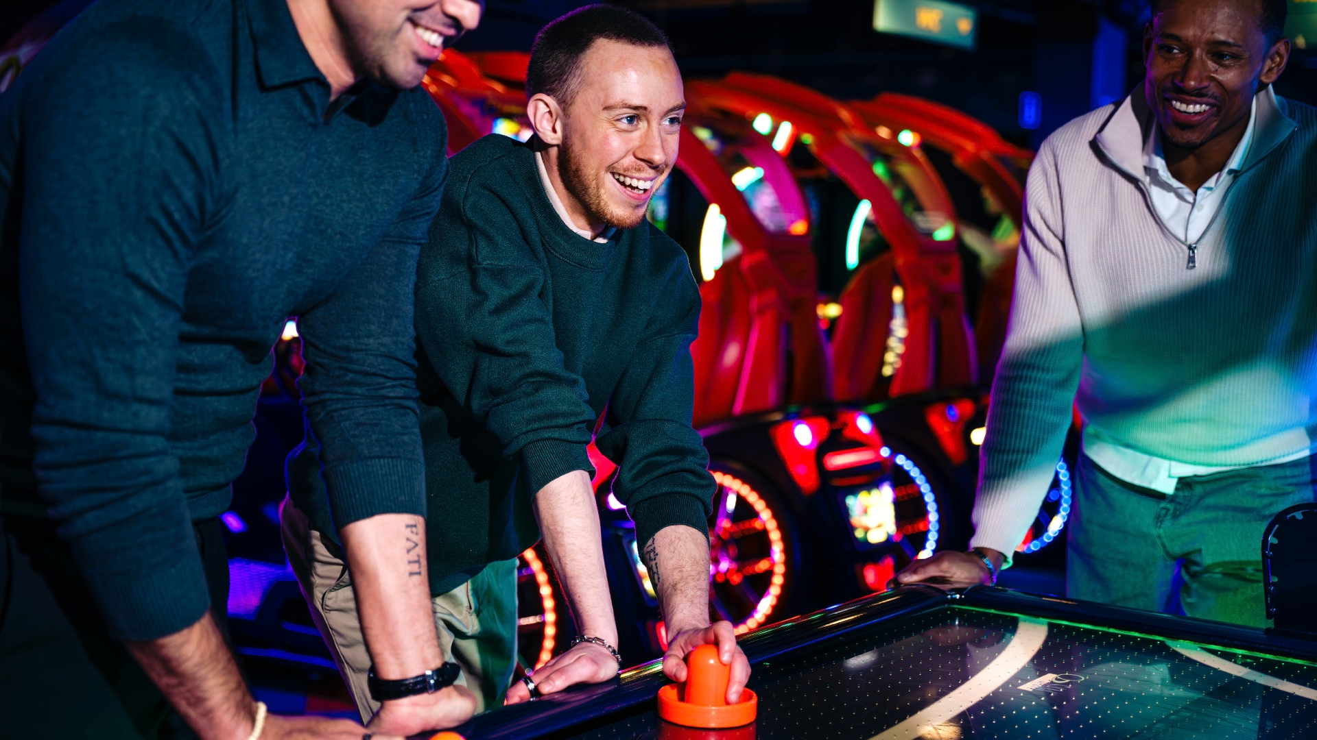 Friends enjoying arcade games and air hockey during a fun night out at an entertainment venue.