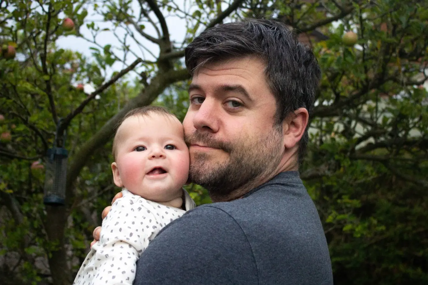 Paul holding his baby with a background of trees