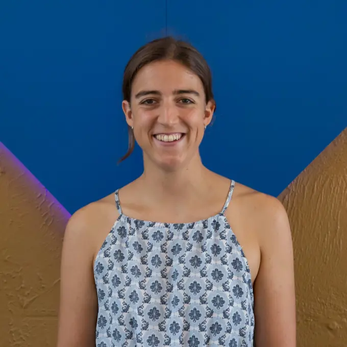 Marina Salvador headshot. Marina has brown hair, is wearing a patterned blue tanktop, and is against a blue and gold background.