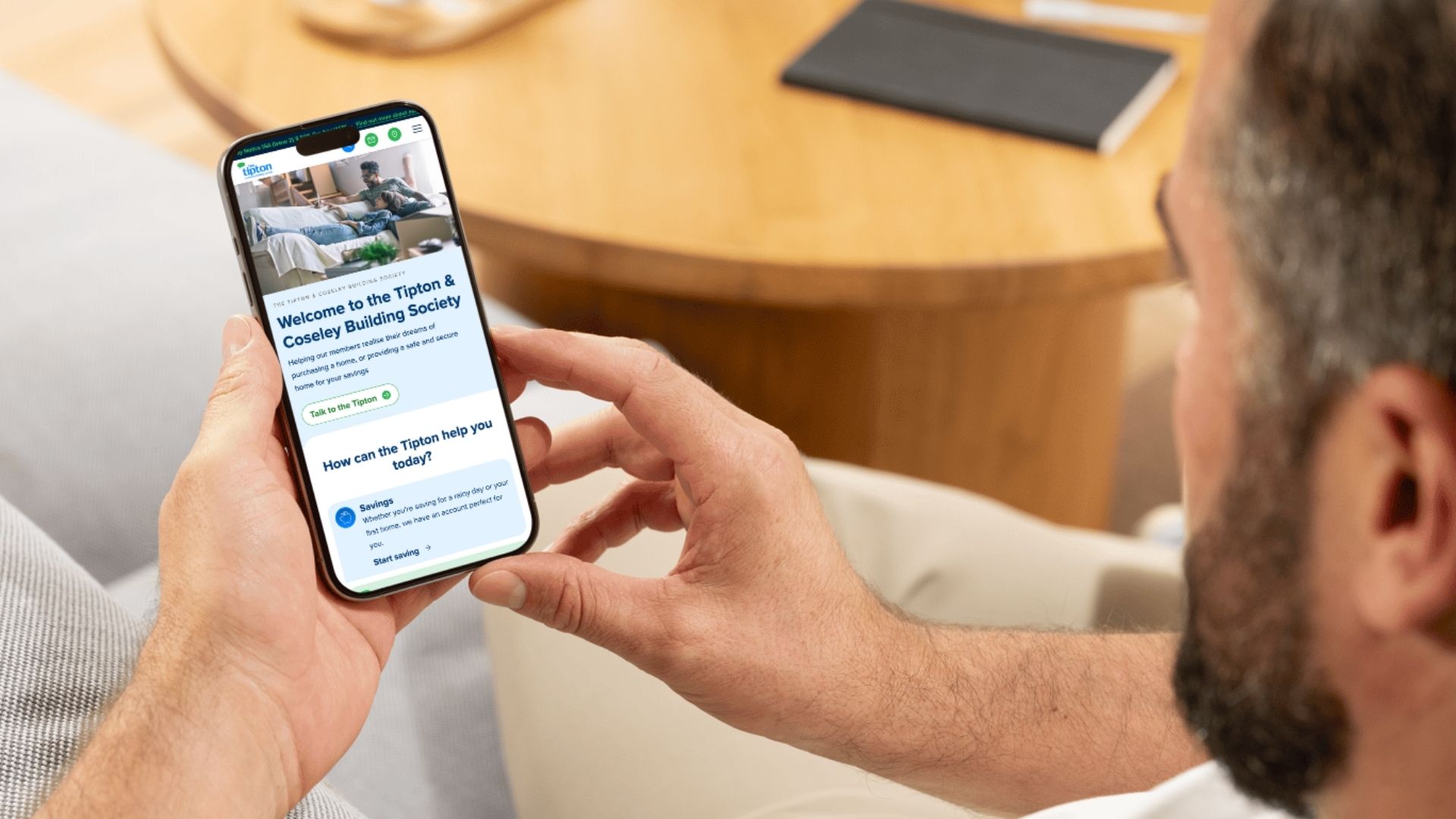 A person holding a smartphone showing the Tipton & Coseley Building Society mobile homepage with a welcome message and a "Start saving" call to action.