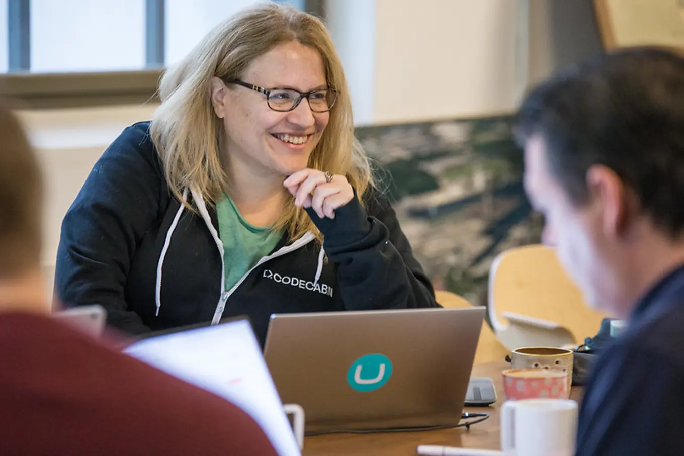 Umbraco developer Lotte Pitcher smiling over a laptop with an Umbraco sticker