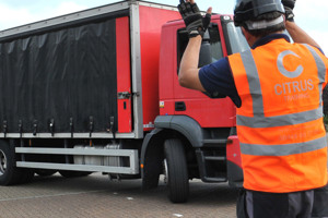 A close-up, real-life photo of a person wearing an orange high-visibility Citrus Training vest and helmet as they guide a large red commercial truck.
