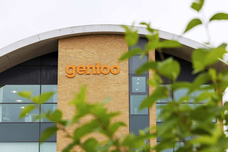gentoO building entrance with brick wall and gold “gentoO” sign, framed by green leaves