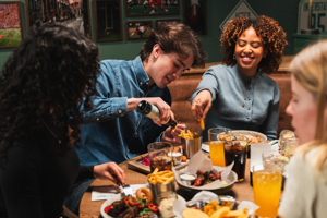 People sitting at a dinner table, pouring drinks and eating fries in a restaurant with framed sports photos behind.