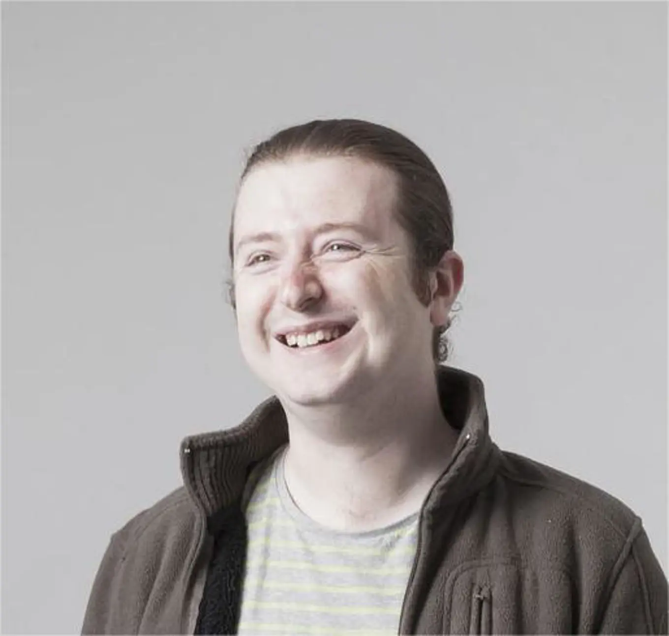 Head shot set against a grey background, of Terence Burridge, wearing pale cream striped top and a brown fleece.